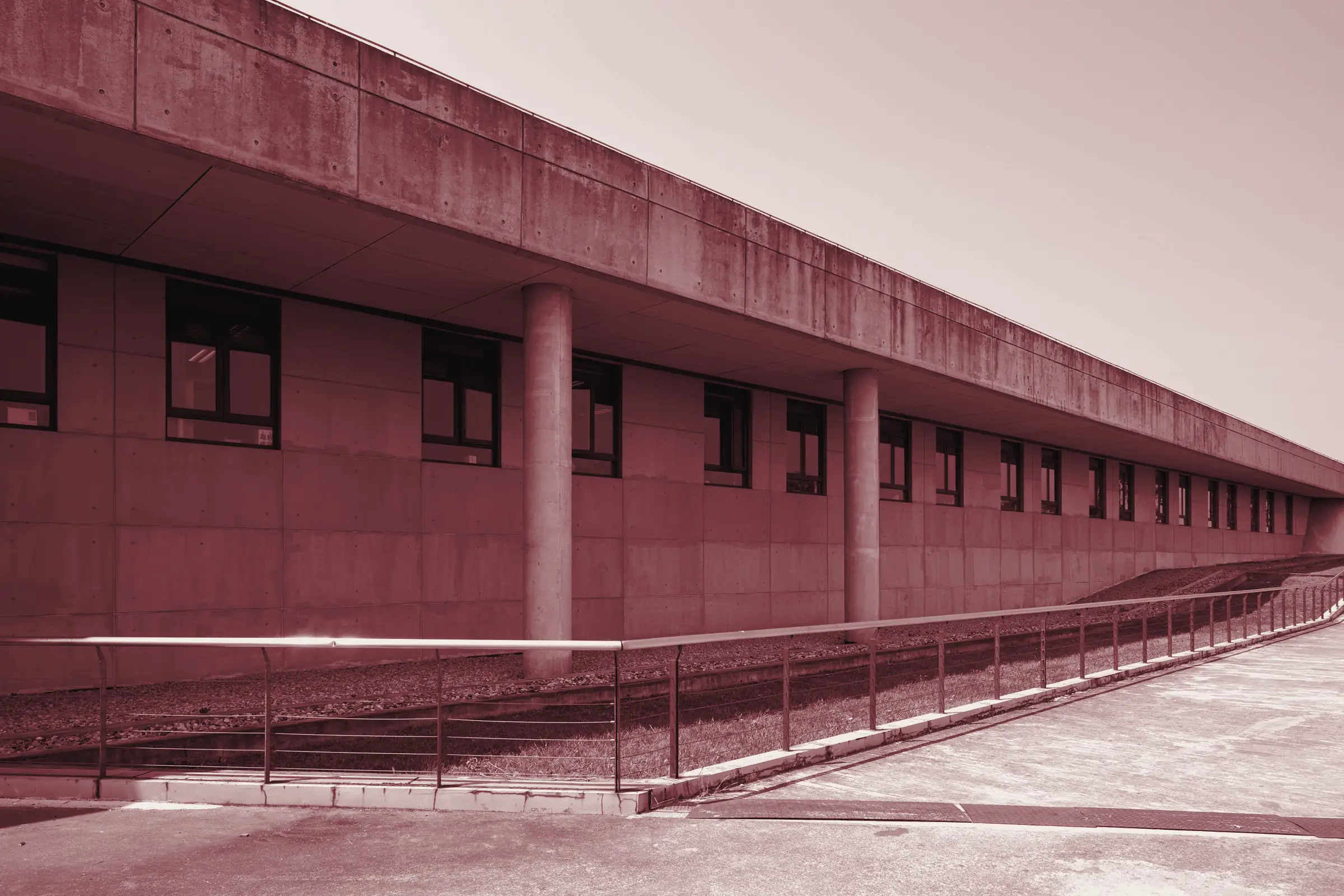 Lunga rampa in cemento con corrimano metallico lungo la facciata di un edificio, sotto un cielo azzurro
