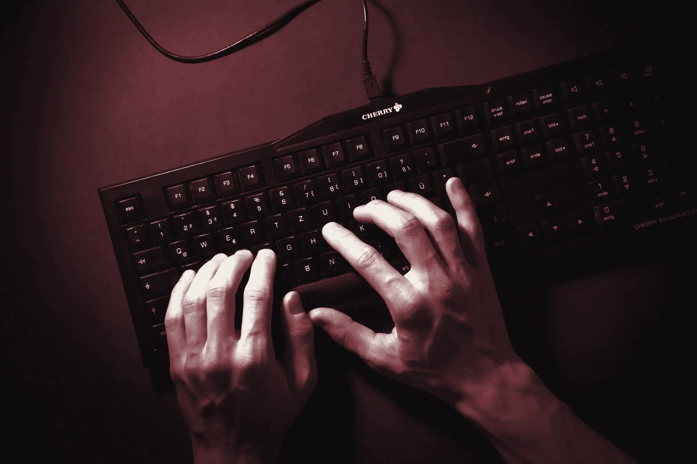 Mani che scrivono su una tastiera nera in una stanza buia