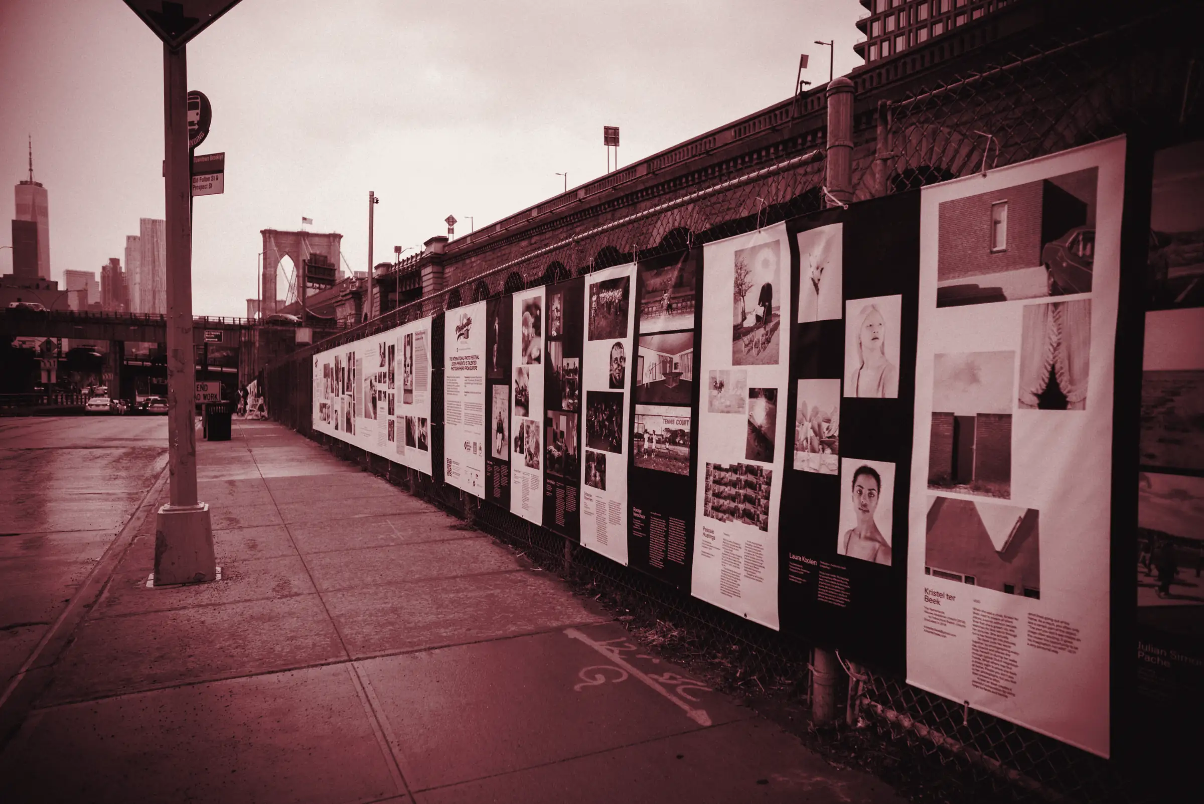 Marciapiede lungo una recinzione coperta di manifesti bianchi e colorati, con prospettiva profonda e lo skyline di una città sullo sfondo