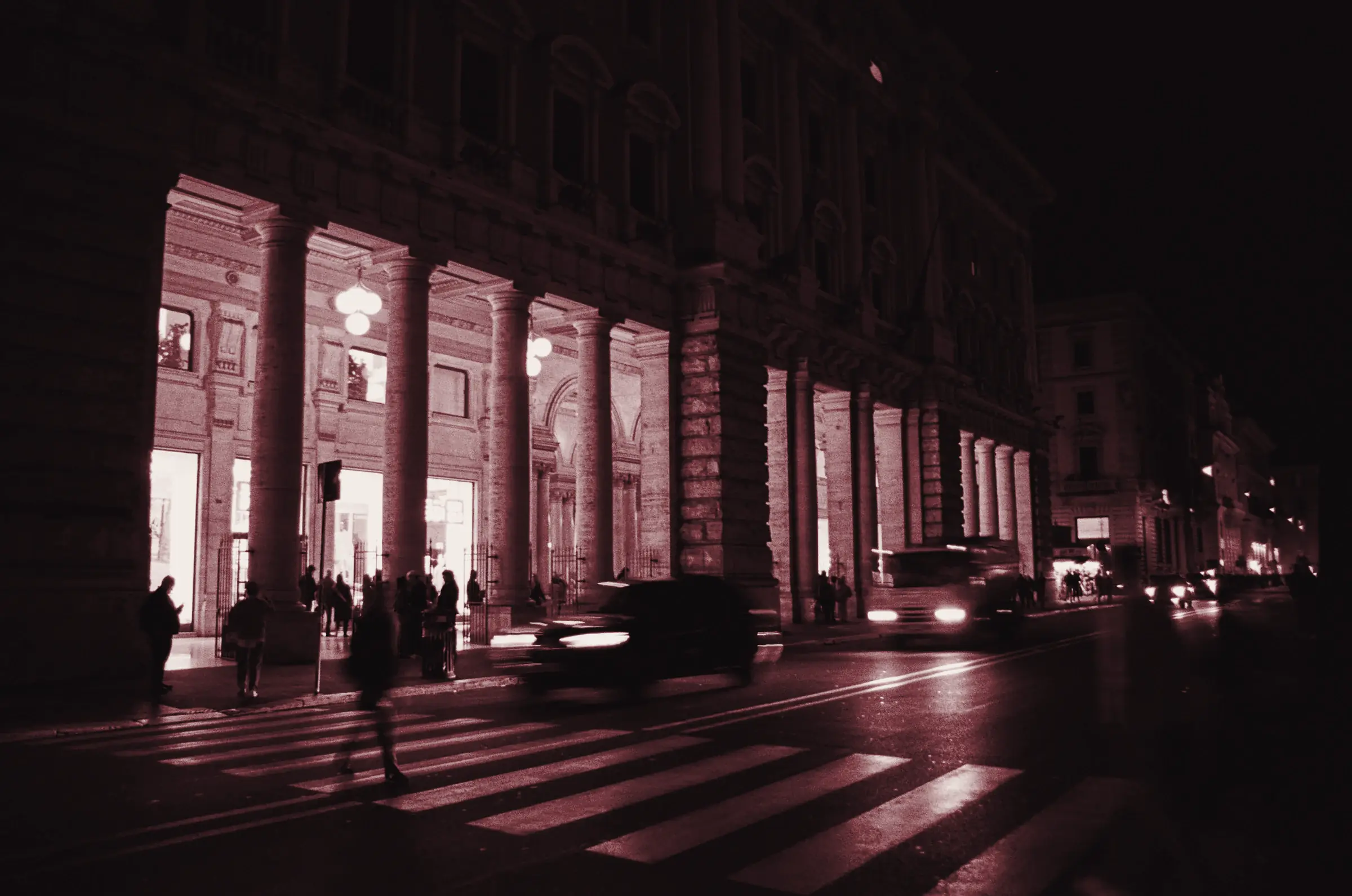 Via di Roma di notte con i portici dei negozi illuminati e le auto in movimento