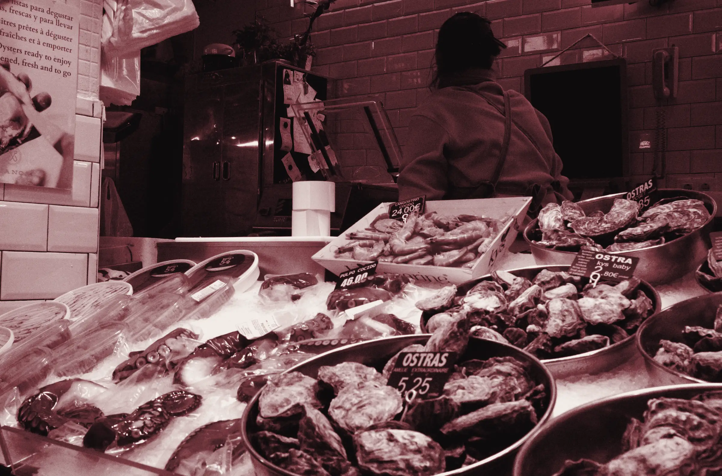 Banco del pesce in un mercato con polpi e ostriche sul ghiaccio, cartellini con prezzi e scritte in più lingue